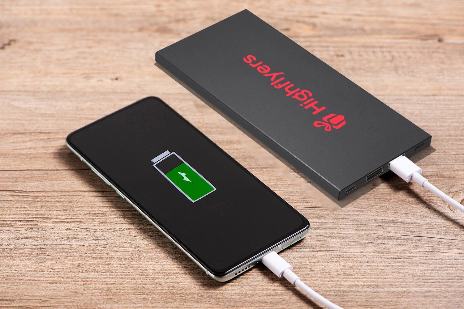 schwarze Powerbank mit Logo neben ladendem Handy