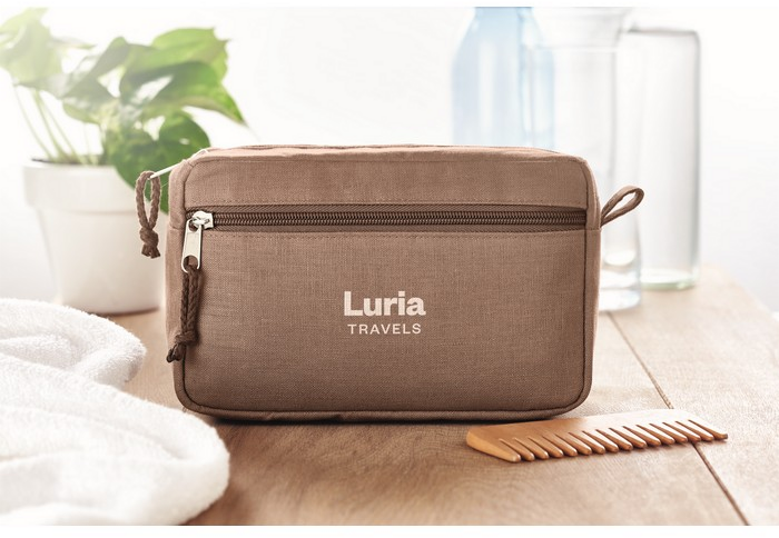 Eine braune Kosmetiktasche steht auf einem Tisch. Der Firmenschriftzug einer Firma ist in weiß mittig auf der Tasche platziert. Die Werbeanbringung wurde im Siebdruck umgesetzt.