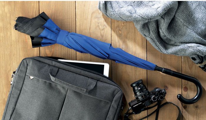 Blauer Stockschirm auf Boden mit Laptoptasche und Kamera.