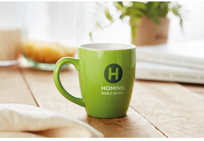 Eine grüne Tasse mit einem zweifarbigen Transferdruck steht auf einem Holztisch.