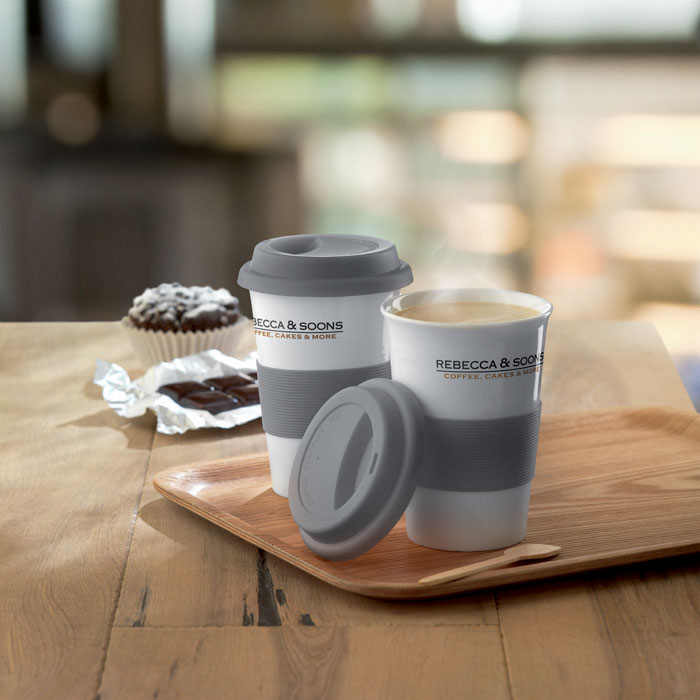 Zwei Keramik To-Go-Becher stehen auf einem Tablet. Beide Becher sind mit einem zweifarbigen Siebdruck Rundum bedruckt.
