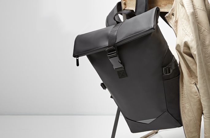 Ein neuer und moderner schwarzer Rolltoprucksack hängt über einem Stuhl.