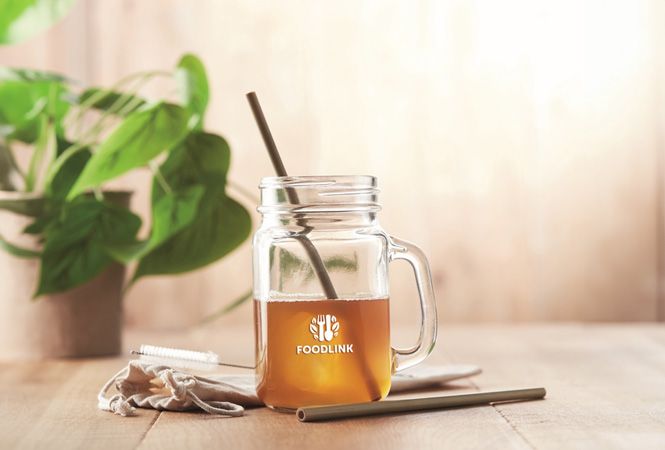 Bambushalm im Glas mit Eistee auf dem Tisch neben einer Pflanze
