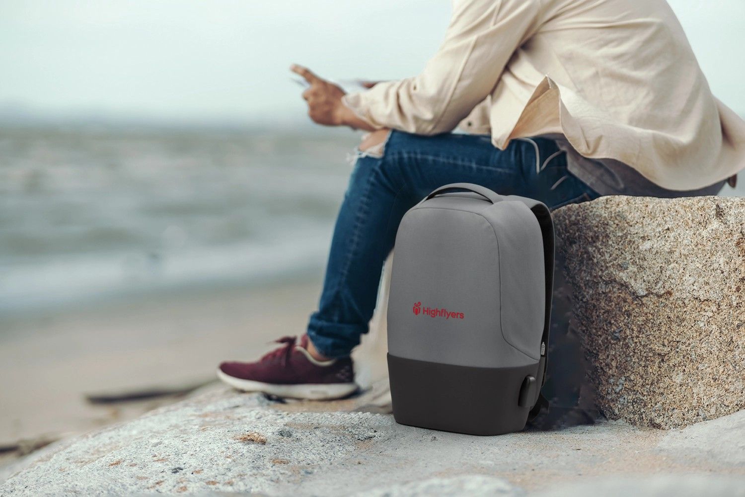 Rucksack lehnt neben Fels auf dem eine Person sitzt