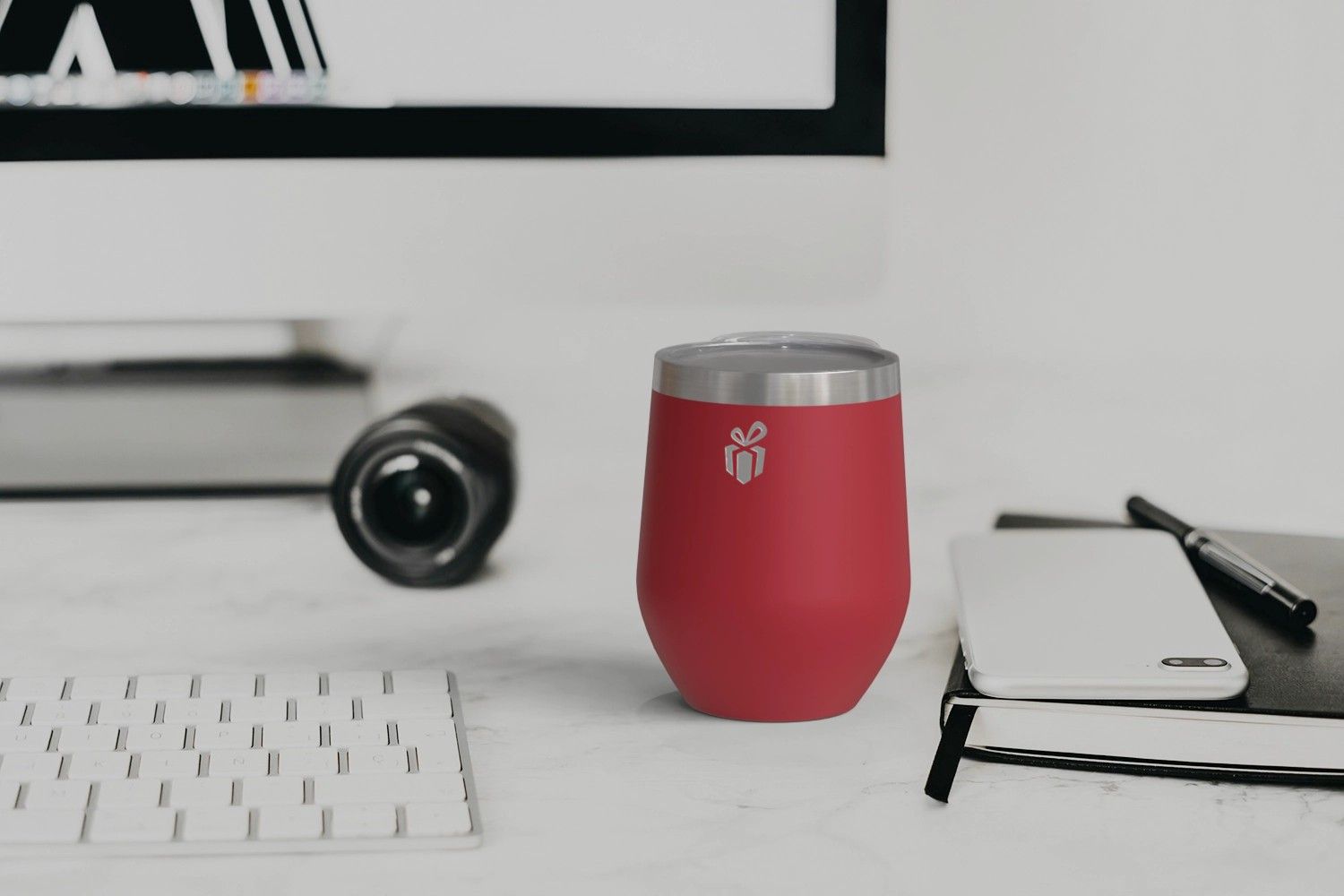 roter Isolierbecher mit Logo auf Schreitisch neben Tastatur