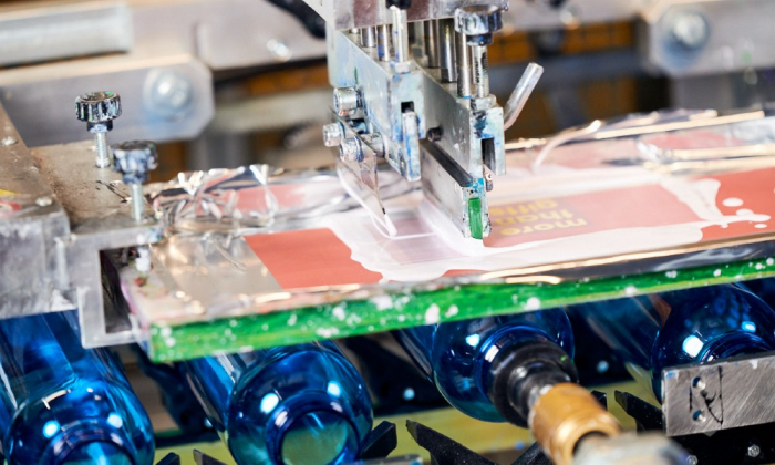 Der Gummirakel einer automatischen Siebdruck Maschine zieht weiße Druckfarbe vom Sieb ab und das gewünschte Druckmotiv wird sichtbar.
