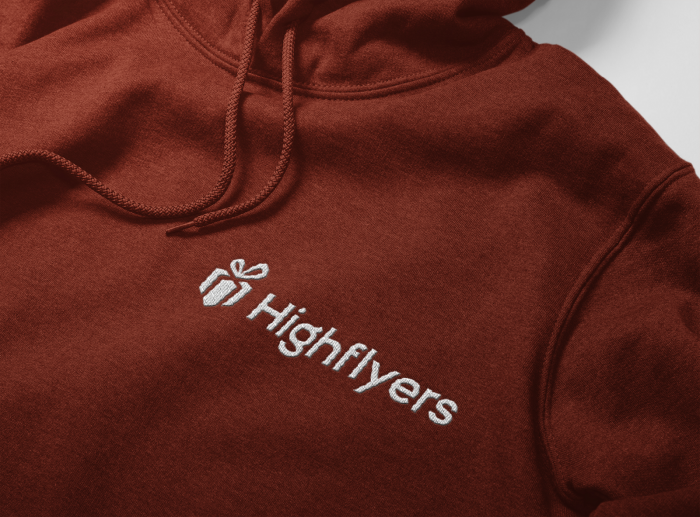 Auf einem roten Kapuzen Hoodie ist in silber das Logo und der Schriftzug der Firma Highflyers Werbeartikel gestickt.